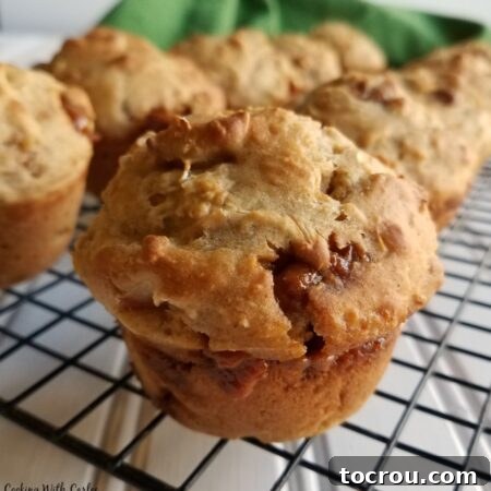 Close up of a freshly baked caramel apple sourdough muffin on a cooling rack, showcasing its melty caramel bits and golden-brown top.