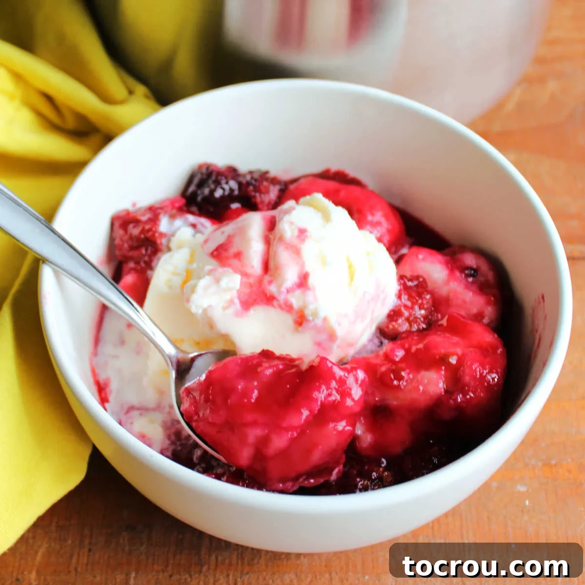 Bowl of blackberry dumplings with vanilla ice cream showing deep purple fluffy dumplings with plenty of sauce and berries.