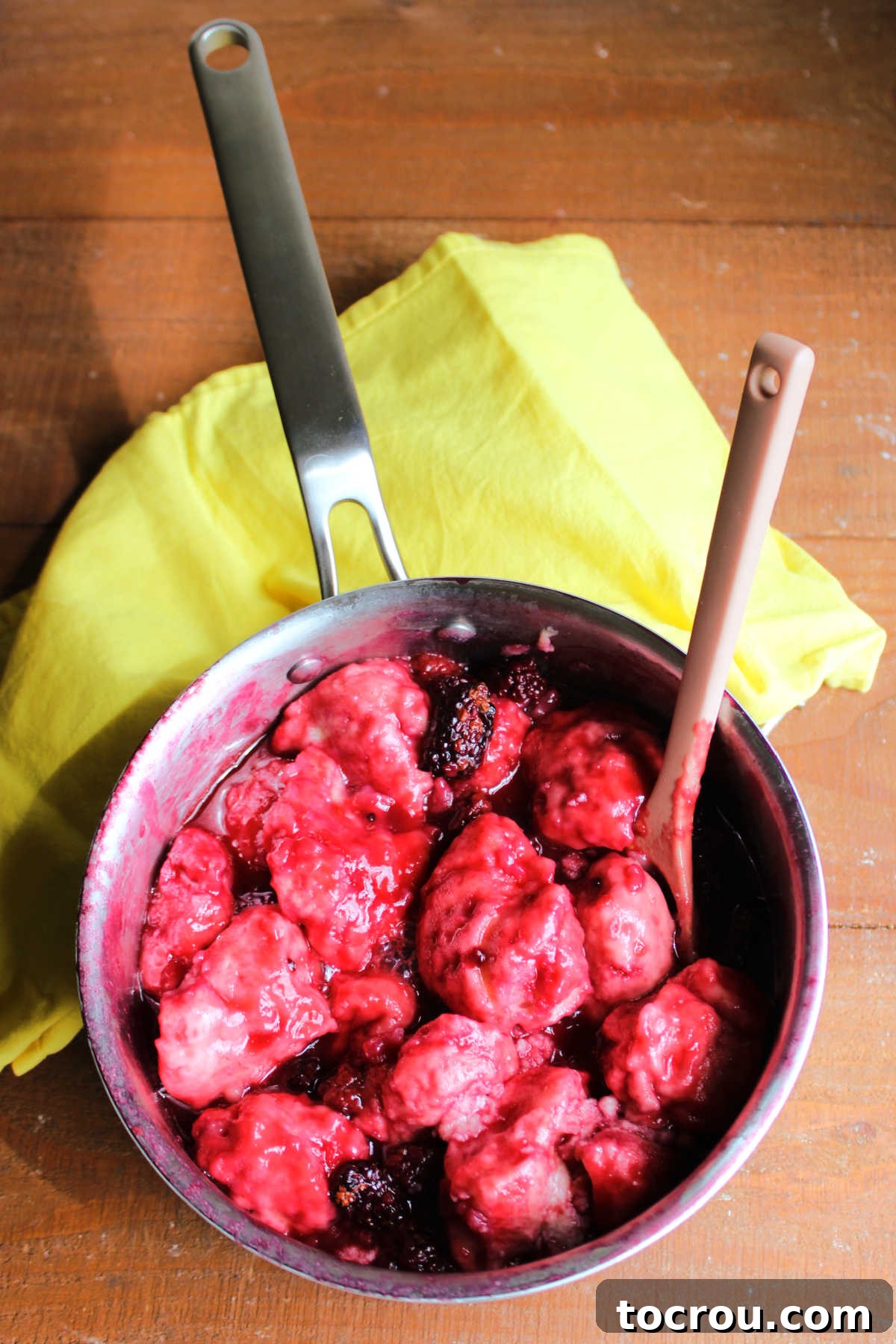 Saucepan filled with soft and fluffy sweet dumplings coated in deep purple blackberry sauce with berries throughout, ready to be served.
