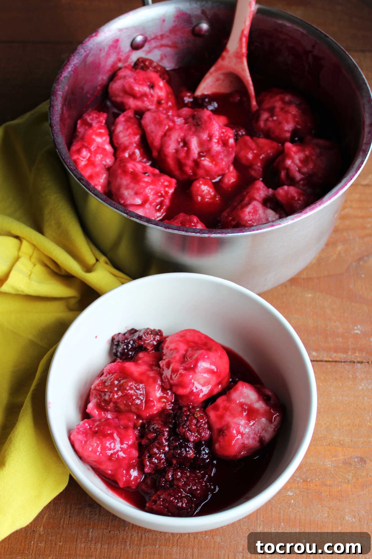 Bowl of blackberry dumplings with lots of sauce and berries by the saucepan it was cooked in.