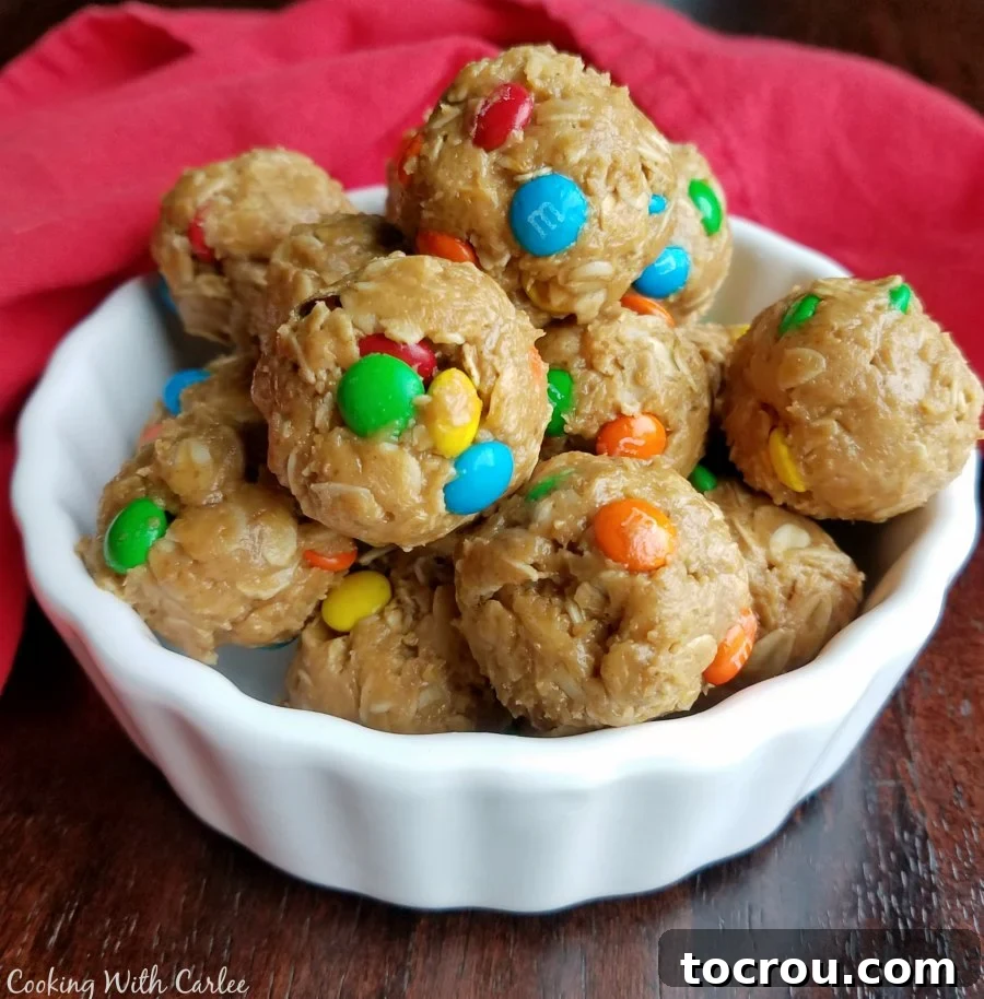 A bowl filled with vibrant monster cookie energy bites, featuring rolled oats, creamy peanut butter, and colorful mini M&Ms. The bites are perfectly round and look irresistible on a clean white surface.