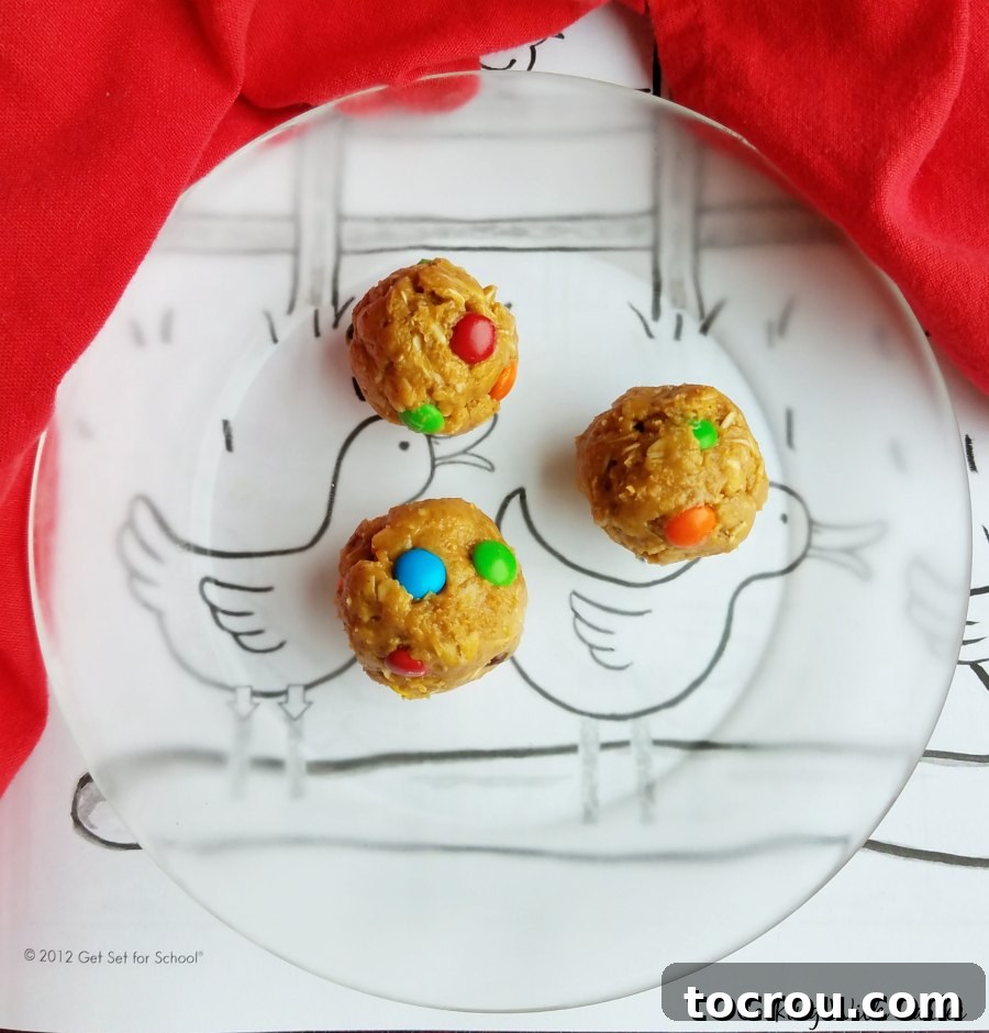 Three perfectly formed monster cookie dough balls rest on a clear glass plate, positioned over a child's coloring page, highlighting their kid-friendly appeal and ease of preparation.