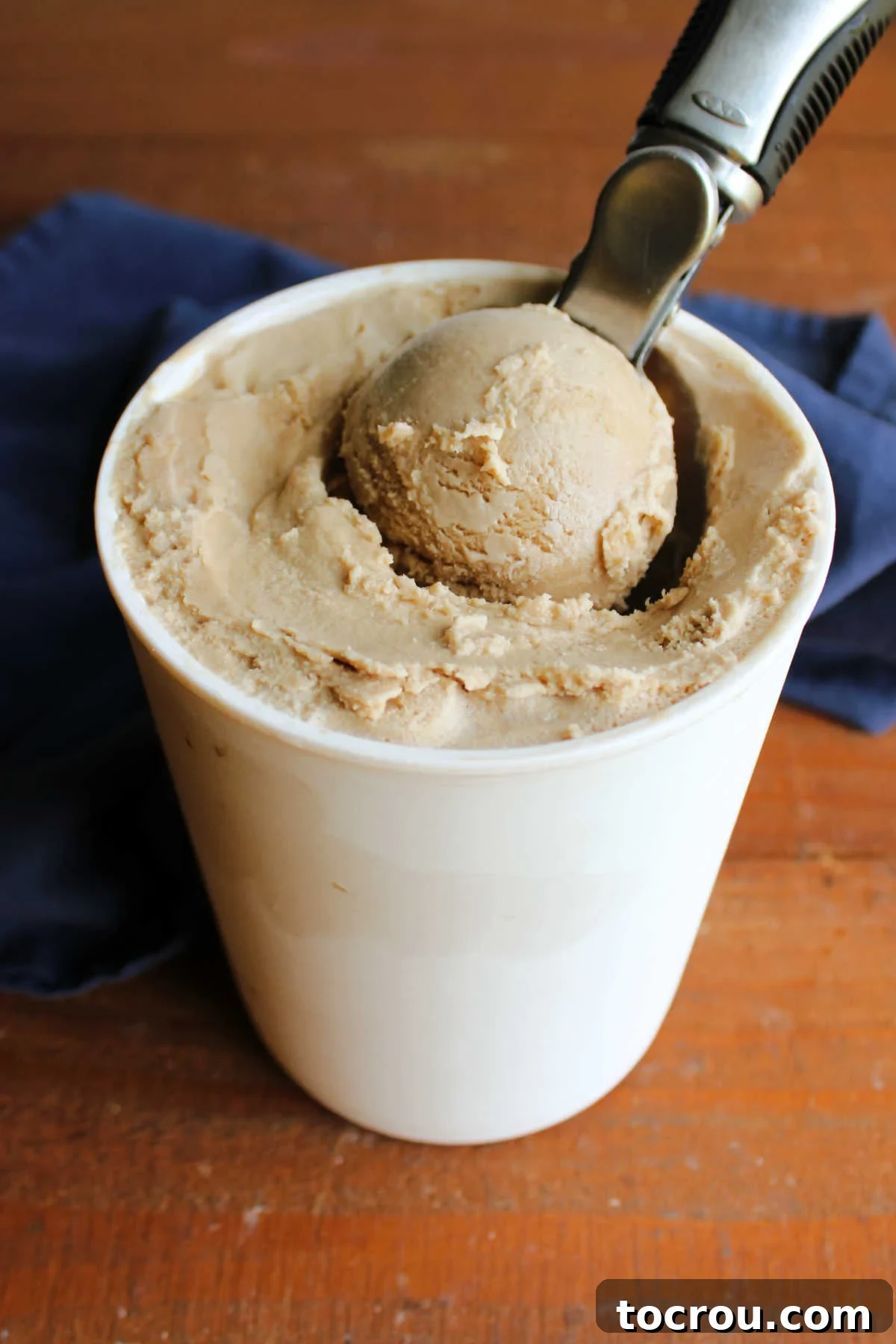 An ice cream scoop carefully lifting a perfect serving of Vietnamese coffee ice cream from a frozen storage container, highlighting its smooth texture.