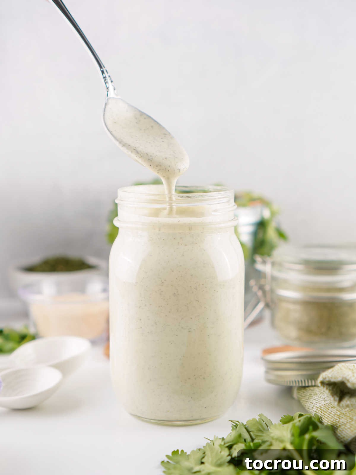 Spoon drizzling some homemade ranch dressing back into the jar it is in. 