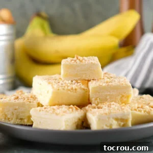 Squares of banana fudge with crushed vanilla wafers on top in front of a bunch of bananas.