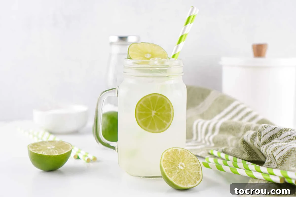 Glass jar filled with ice and lime shake up mixture with extra lime halves and straws nearby. 