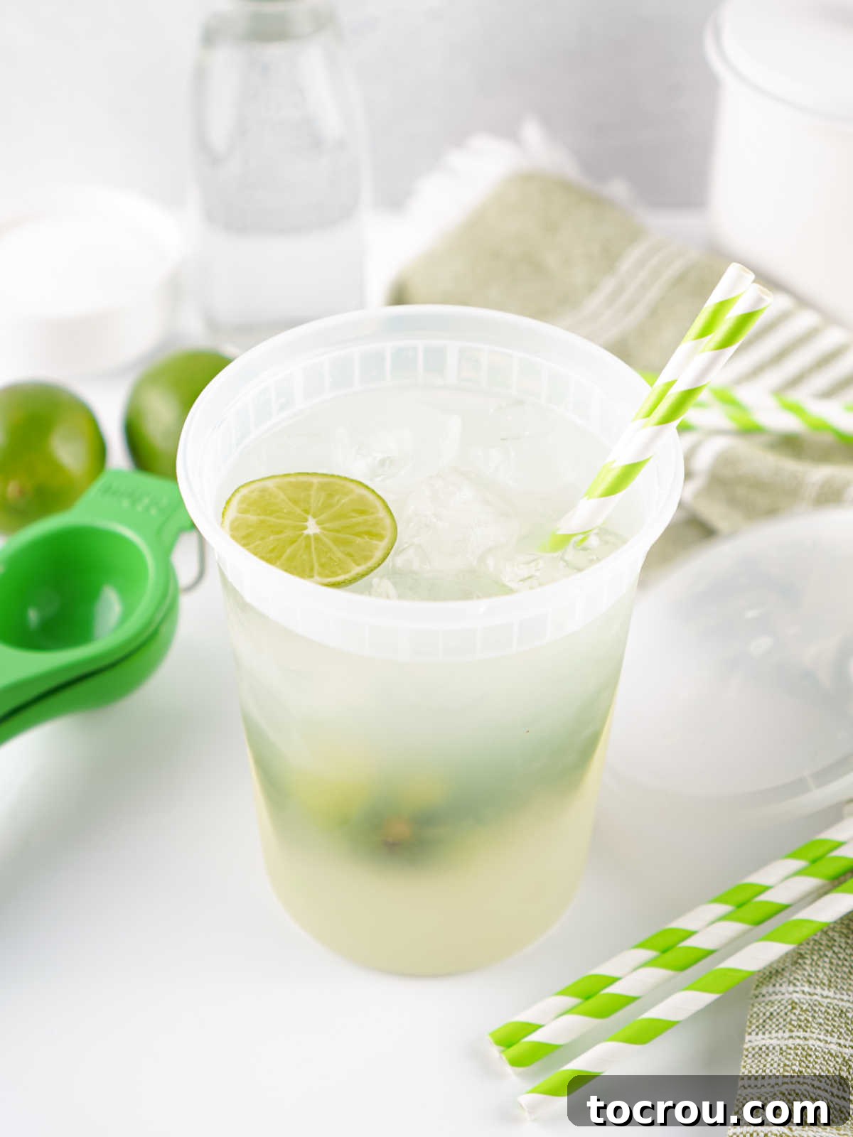 Plastic deli container filled with lime shake up, ice, and a paper straw. 
