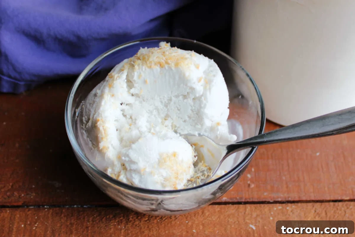 Spoon getting a bite of homemade coconut ice cream topped with toasted shredded coconut.