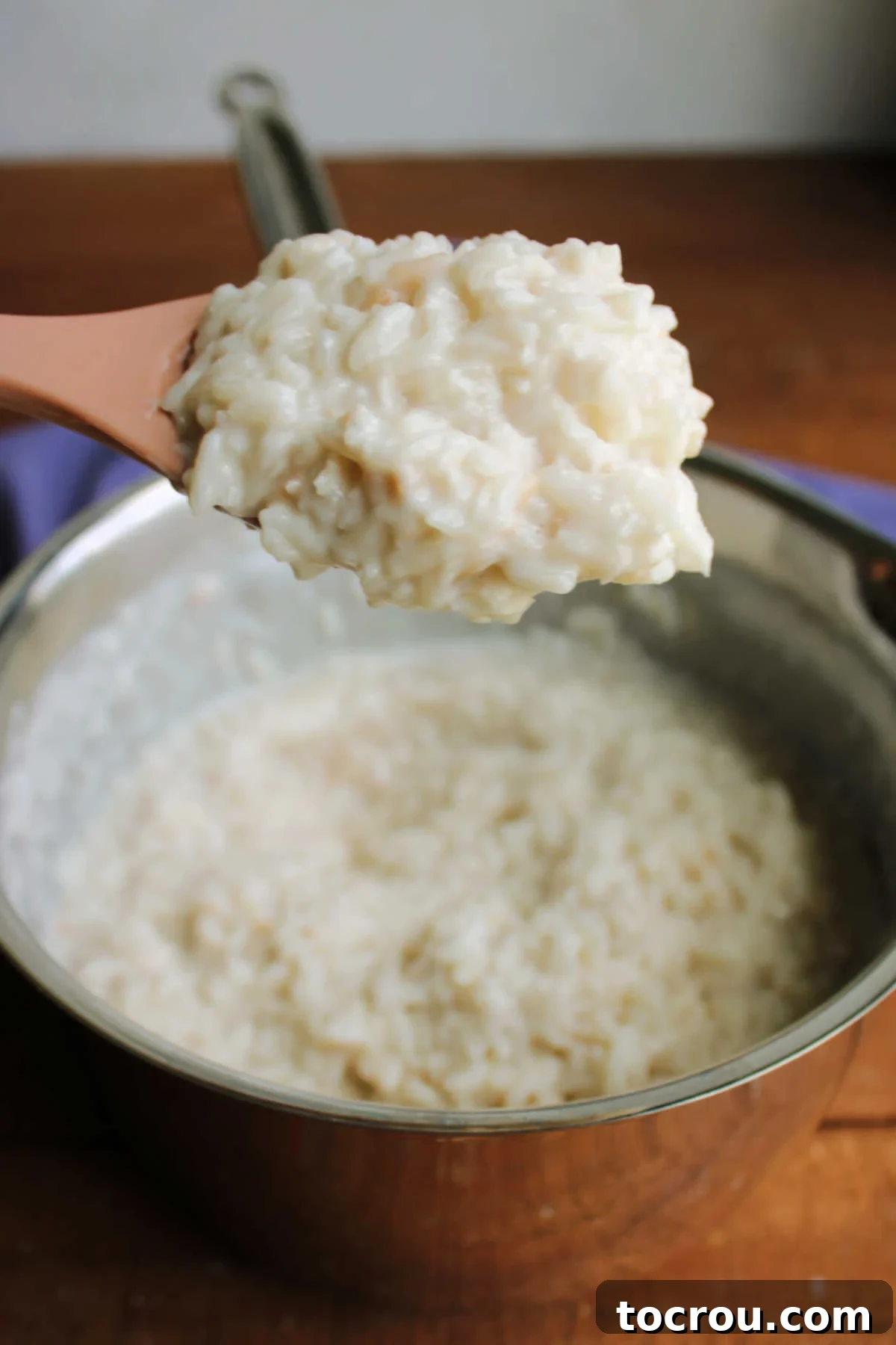 A serving spoon captures a scoop of creamy coconut rice pudding directly from the cooking pan, highlighting its appealing texture.