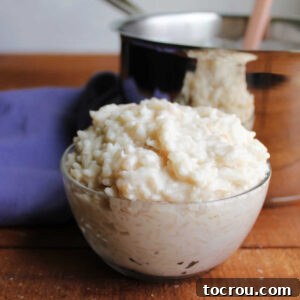 Small glass bowl of coconut rice pudding in front of the saucepan it was cooked in.