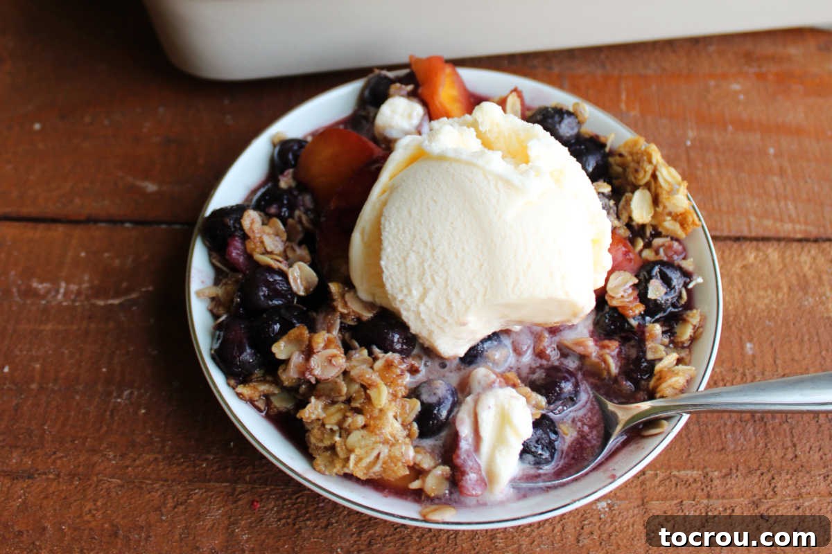 Homemade Blueberry Peach Crisp with Vanilla Ice Cream Bowl of peach blueberry crisp topped with scoop of vanilla ice cream, ready to eat.