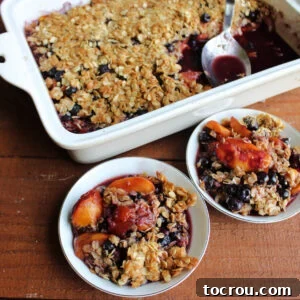 Two small dishes of peach blueberry crisp with baking pan of remaining dessert in the background.