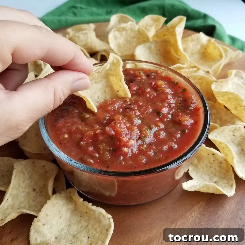 Delicious Roasted Salsa Hand dipping a tortilla chip into a bowl of fresh, homemade roasted salsa, showcasing its rich texture and vibrant color.