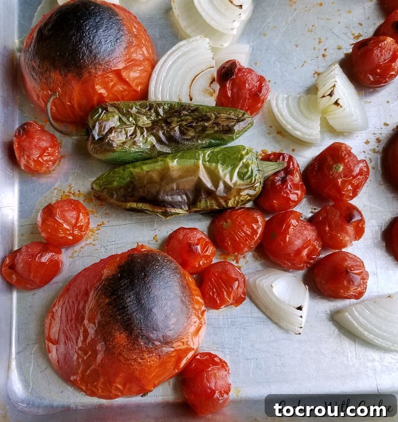 Roasted Vegetables for Salsa Sheet pan filled with charred tomatoes, onions, and jalapeños, fresh from the oven and ready to be blended into salsa.