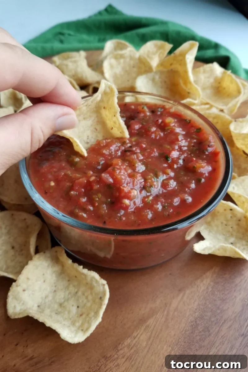 Enjoying Roasted Salsa A hand scooping thick, homemade roasted salsa from a glass bowl with a tortilla chip.