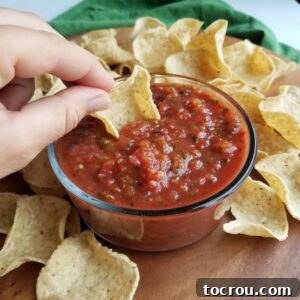 Roasted Salsa hand dipping tortilla chip into bowl of fresh roasted salsa.