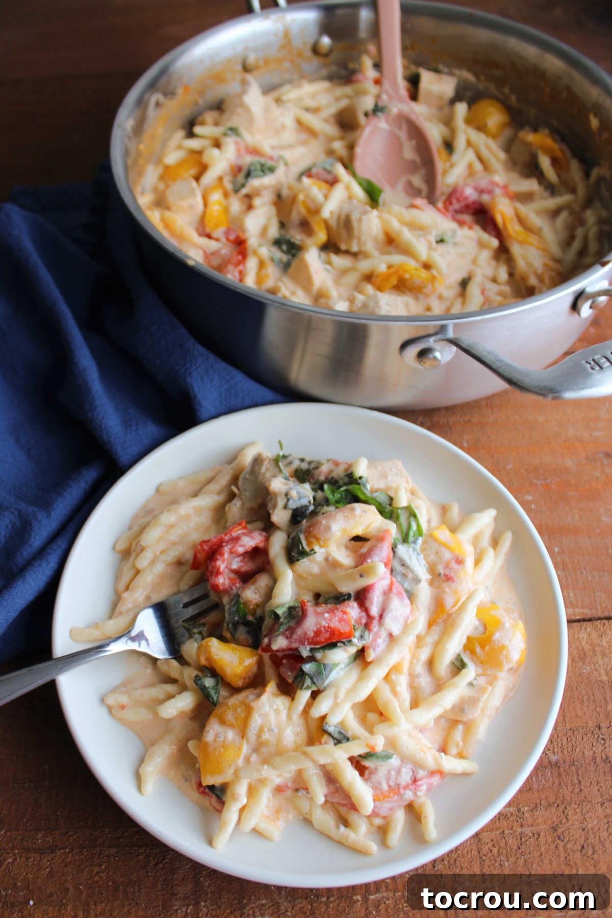 Fork getting bite of baked feta pasta with tomatoes, chicken, and basil.
