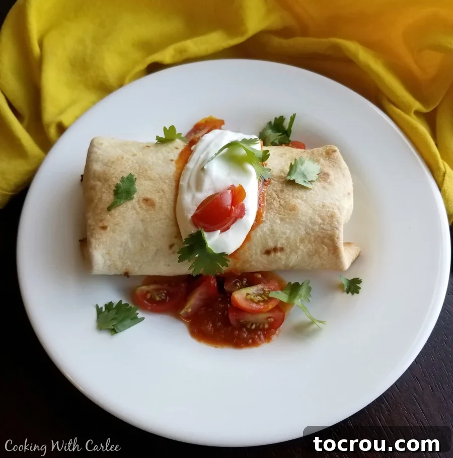 Crispy Baked Breakfast Chimichangas with Eggs, Ham, Cheese, and Potato Baked breakfast chimichanga with sour cream, tomatoes and cilantro on top, served on a plate.