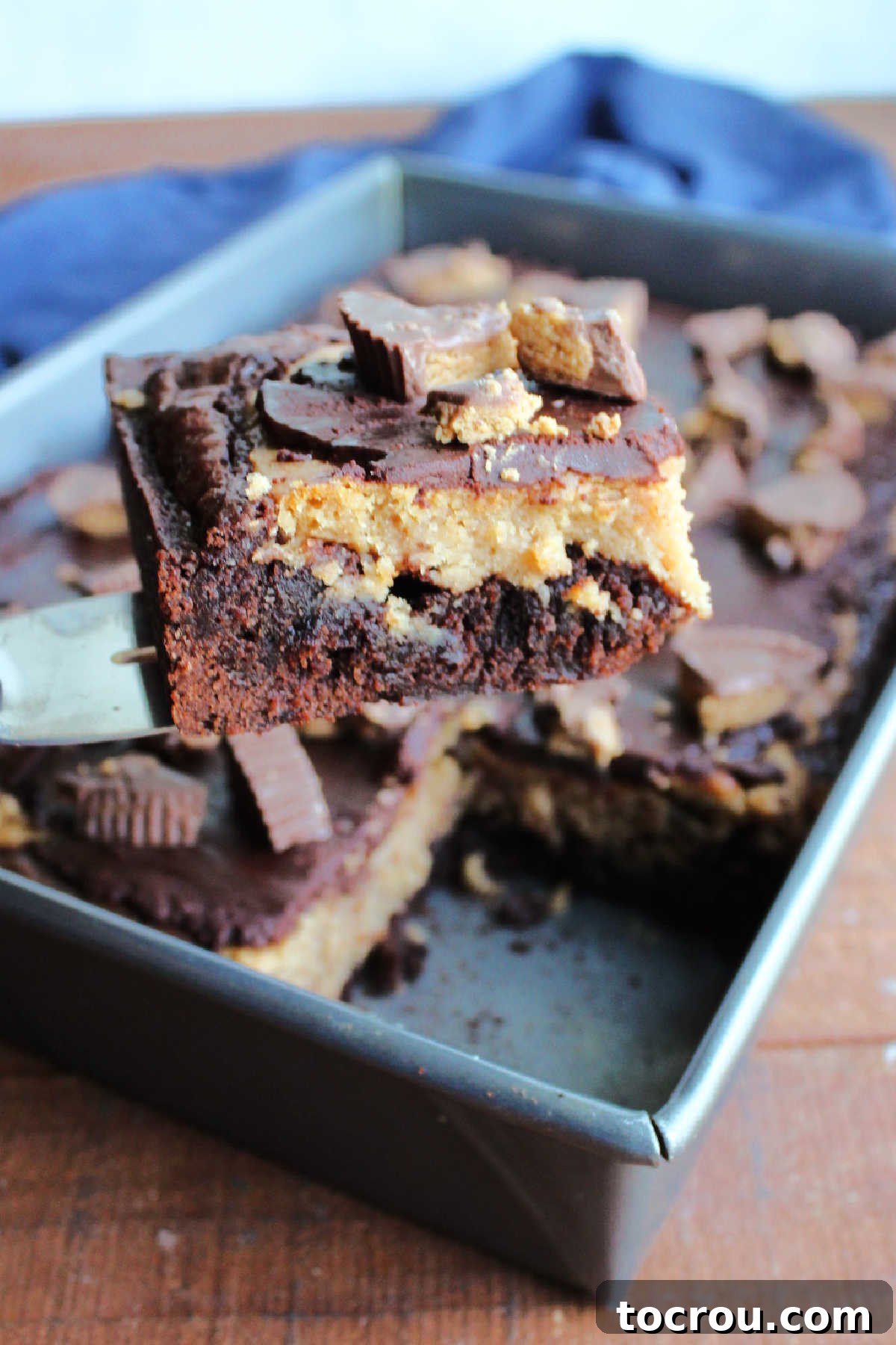 A spatula carefully lifting a perfectly cut square of peanut butter cheesecake brownie out of a pan, ready to be served and enjoyed.