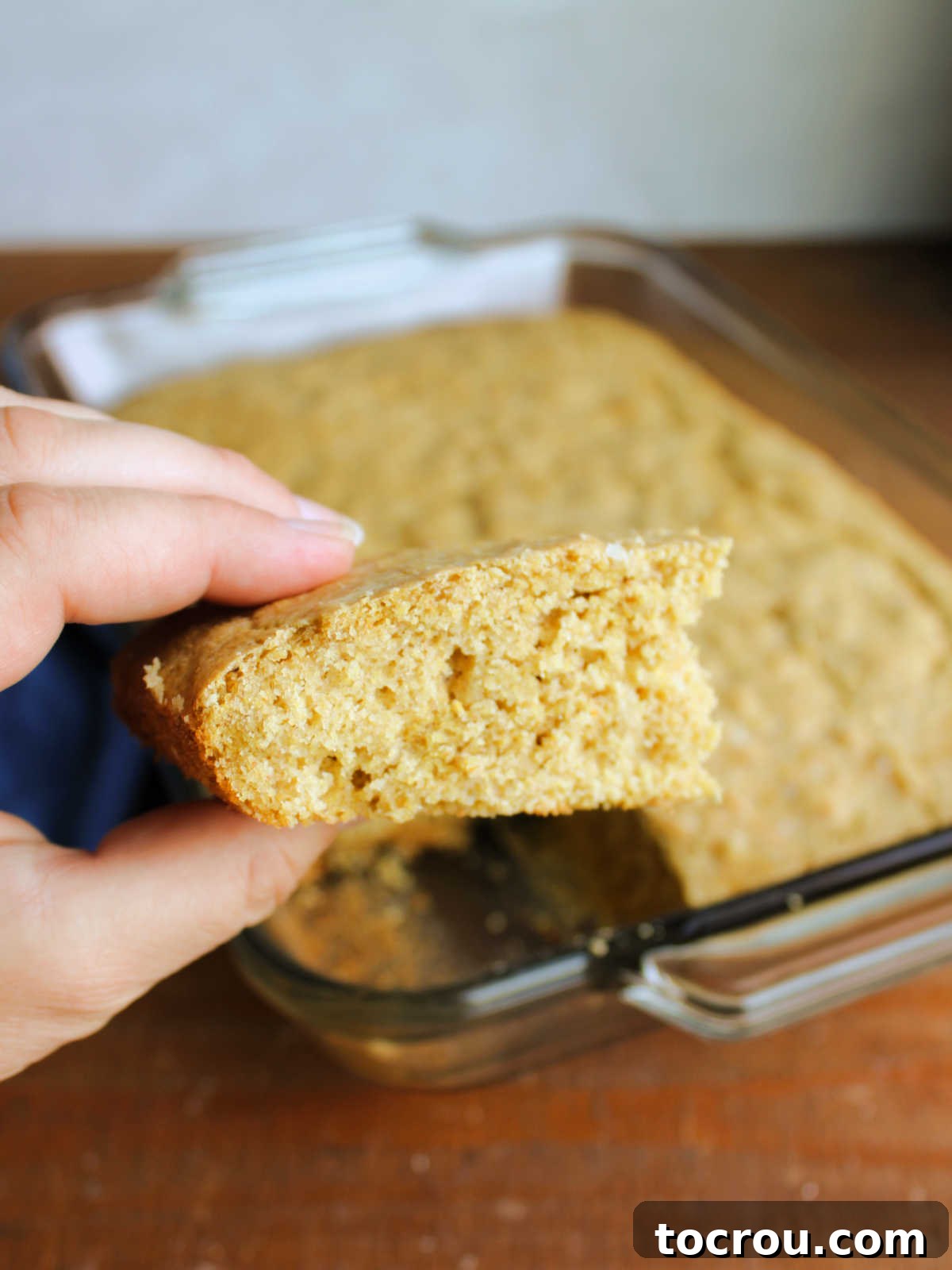 Hand holding piece of sourdough cornbread showing airy texture and moist crumb.