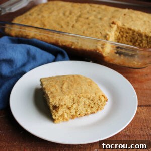 Piece of whole wheat sourdough cornbread on plate with pan of cornbread in the background.