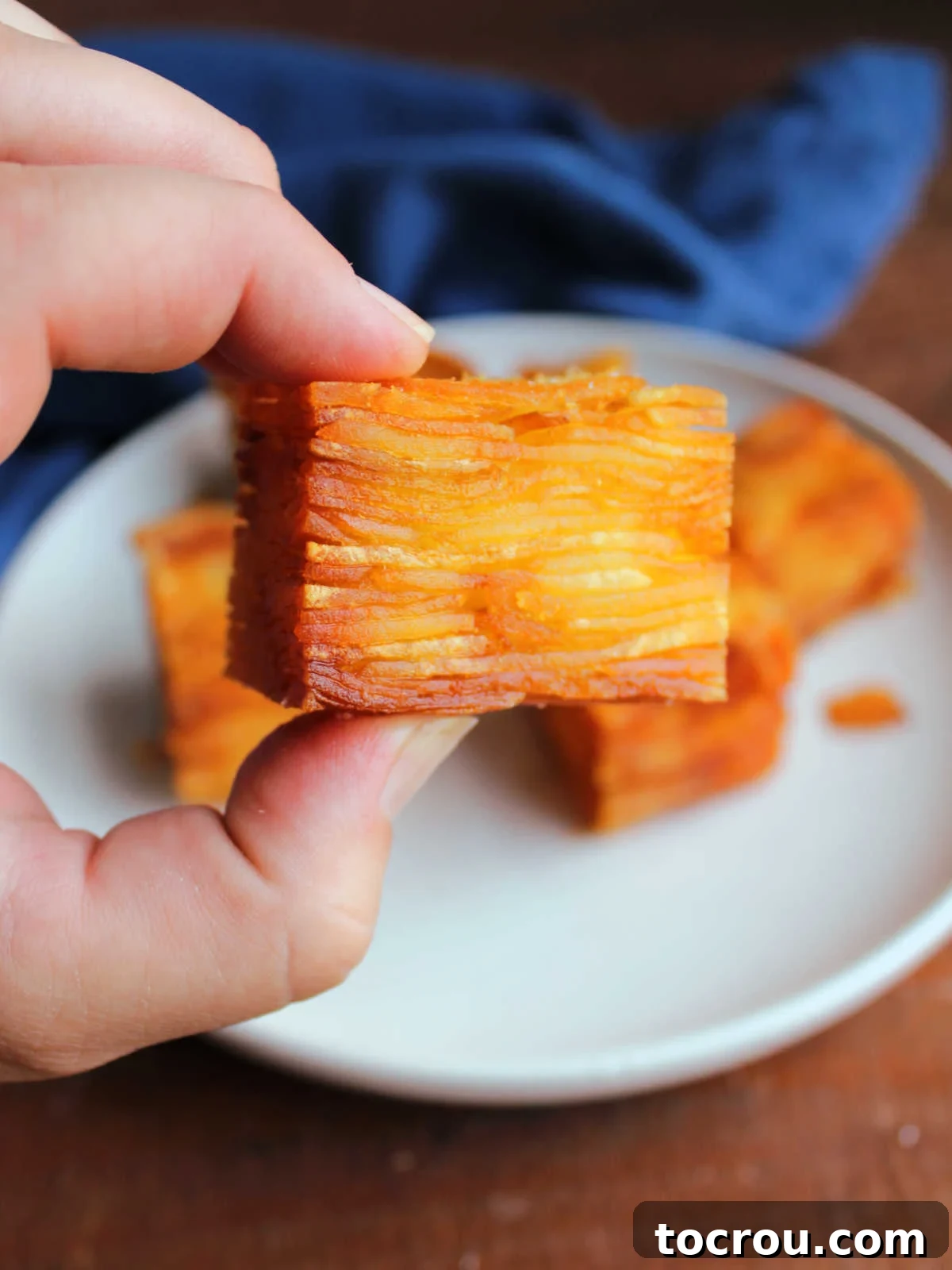 Hand holding a cube of thousand layer potato showing the thin layers of potatoes and gold brown exterior.