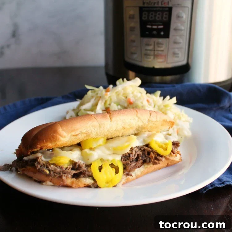 Plate with an Italian beef sandwich with melted provolone and sliced pickled banana peppers on top served with coleslaw in front of an Instant Pot.