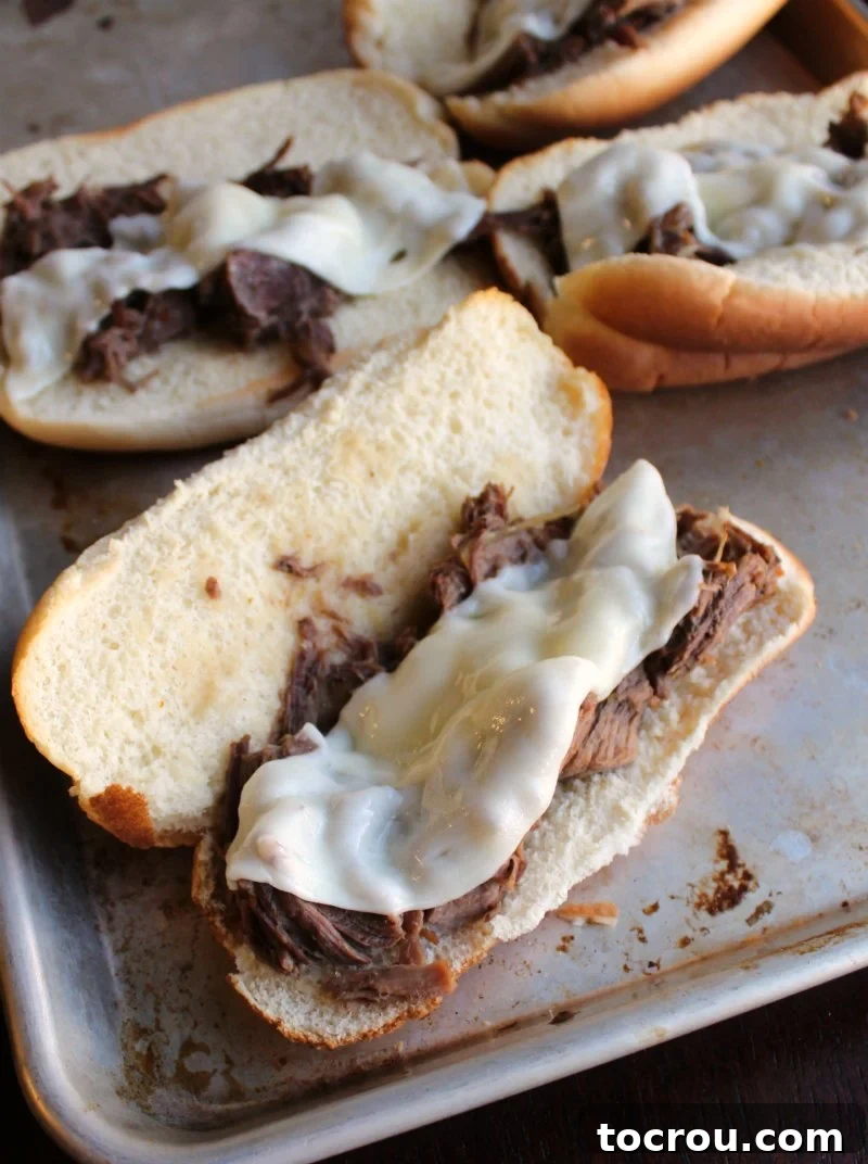 Tray of Italian beef sandwiches with sliced provolone cheese on it fresh from the oven.