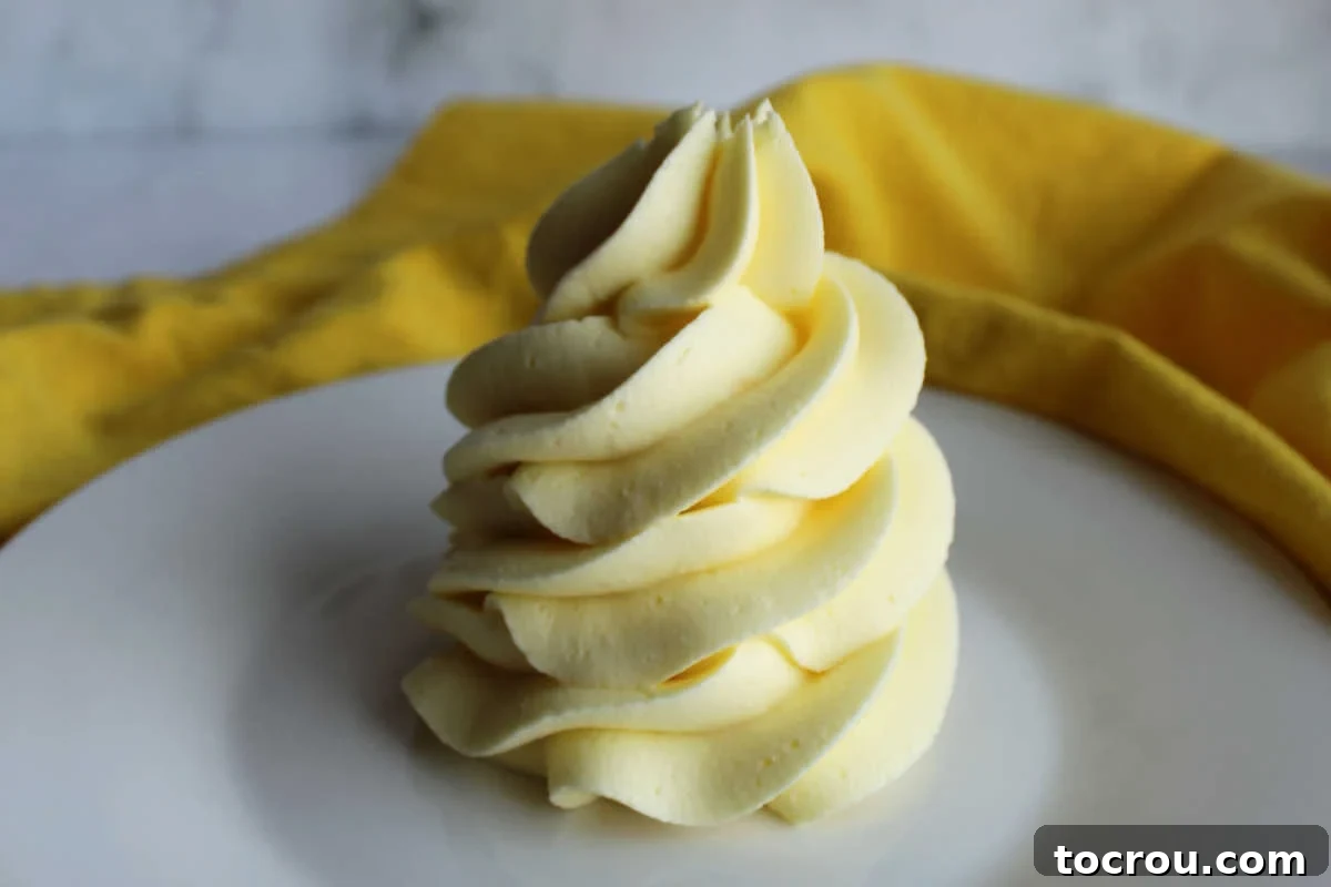 Lemon Condensed Milk Buttercream Swirl A beautifully piped swirl of pale yellow lemon condensed milk buttercream frosting on a pristine plate, showcasing its smooth, sturdy, and inviting texture.