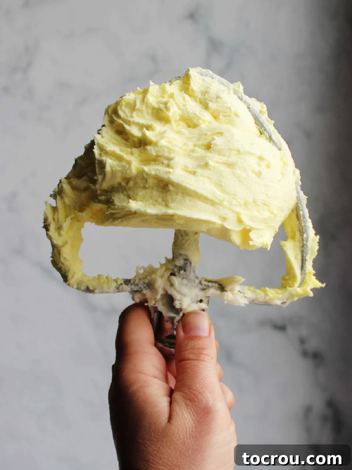 Frosting on Mixer Paddle A mixer paddle, generously coated with the bright yellow lemon condensed milk frosting, showcasing its thick, creamy, and spreadable consistency, ready to adorn any dessert.