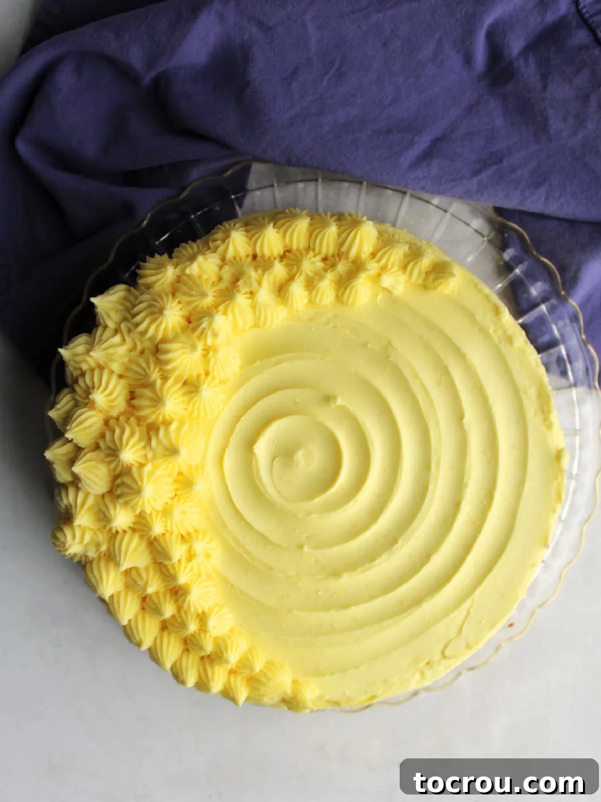 Lemon Velvet Cake with Buttercream A beautifully decorated round lemon velvet cake, elegantly adorned with delicate crescent moon swirls of vibrant lemon condensed milk buttercream frosting on its top surface, creating an inviting and artistic presentation.