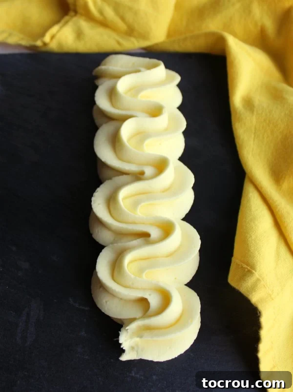 Piped Lemon Buttercream Swirl An artistic swirl of delicate, perfectly piped lemon buttercream frosting, with its light yellow hue and smooth texture, contrasting elegantly against a dark slate background. This image highlights the frosting's ideal consistency for piping and decorating.