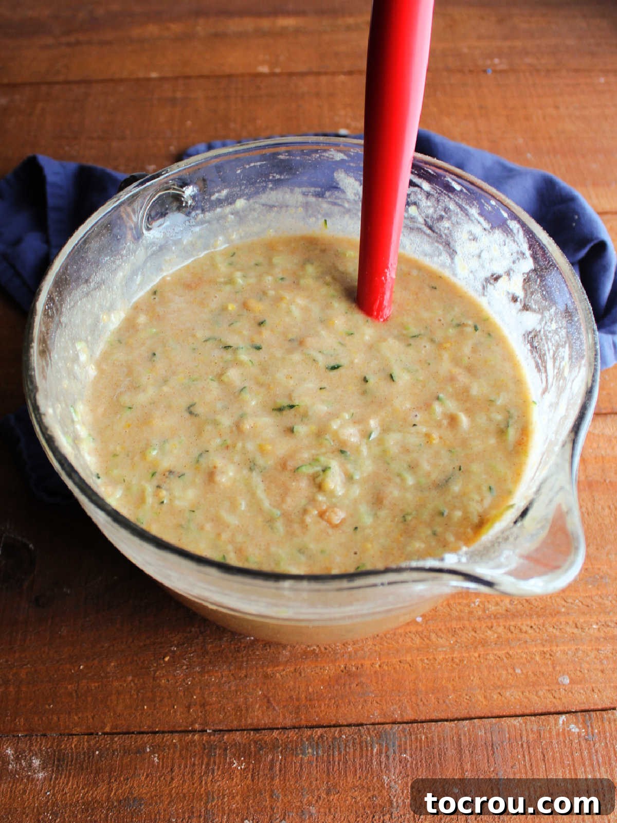Glass mixing bowl filled with smooth zucchini bread batter, ready to be poured into prepared loaf pans.