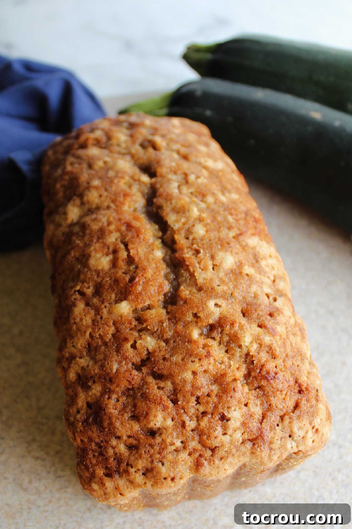 Whole loaf of golden-brown zucchini bread with a slightly crunchy, cinnamon-sugar top, resting on a cooling rack.