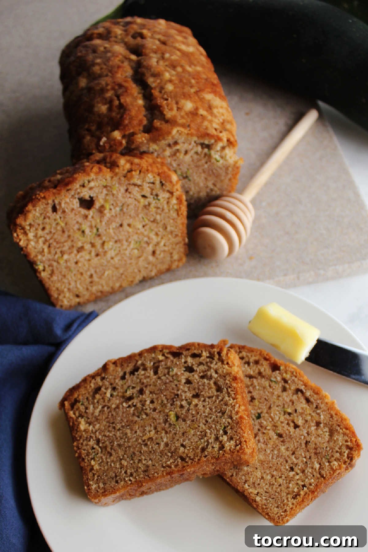 Perfectly sliced zucchini bread, with a knife spreading a dollop of soft butter on a piece, highlighting its moist texture.