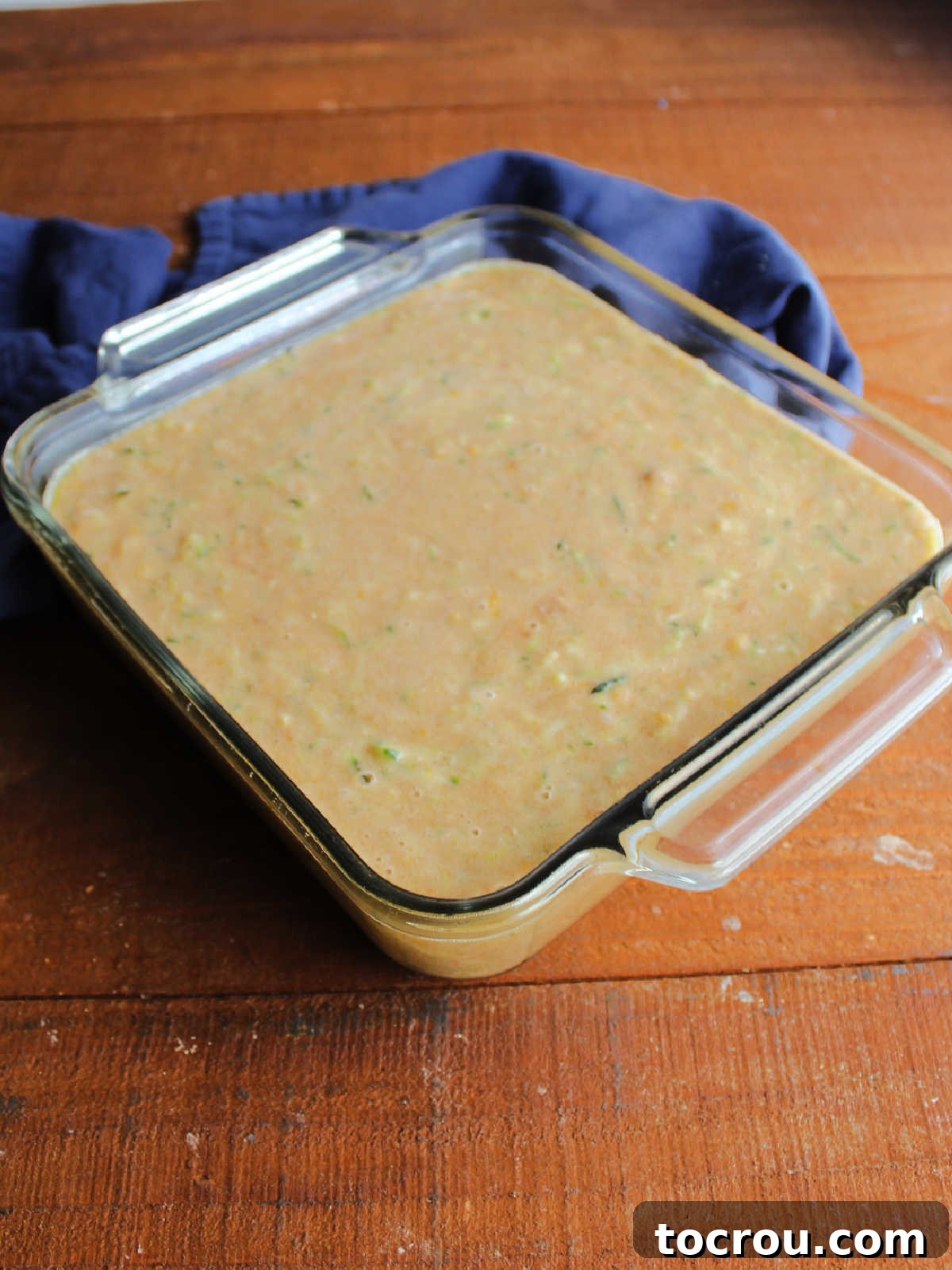 Square baking dish filled with thick zucchini bread batter, smoothly spread and ready to be placed in the oven.