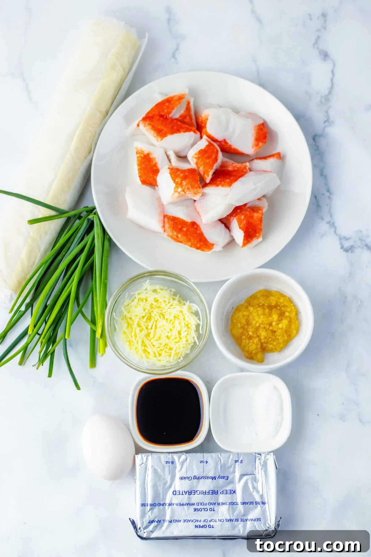 Ingredients including imitation crab, cream cheese, mozzarella cheese, soy sauce, garlic, sugar, chives, and puffy pastry ready to be made into crab rangoon pinwheels.