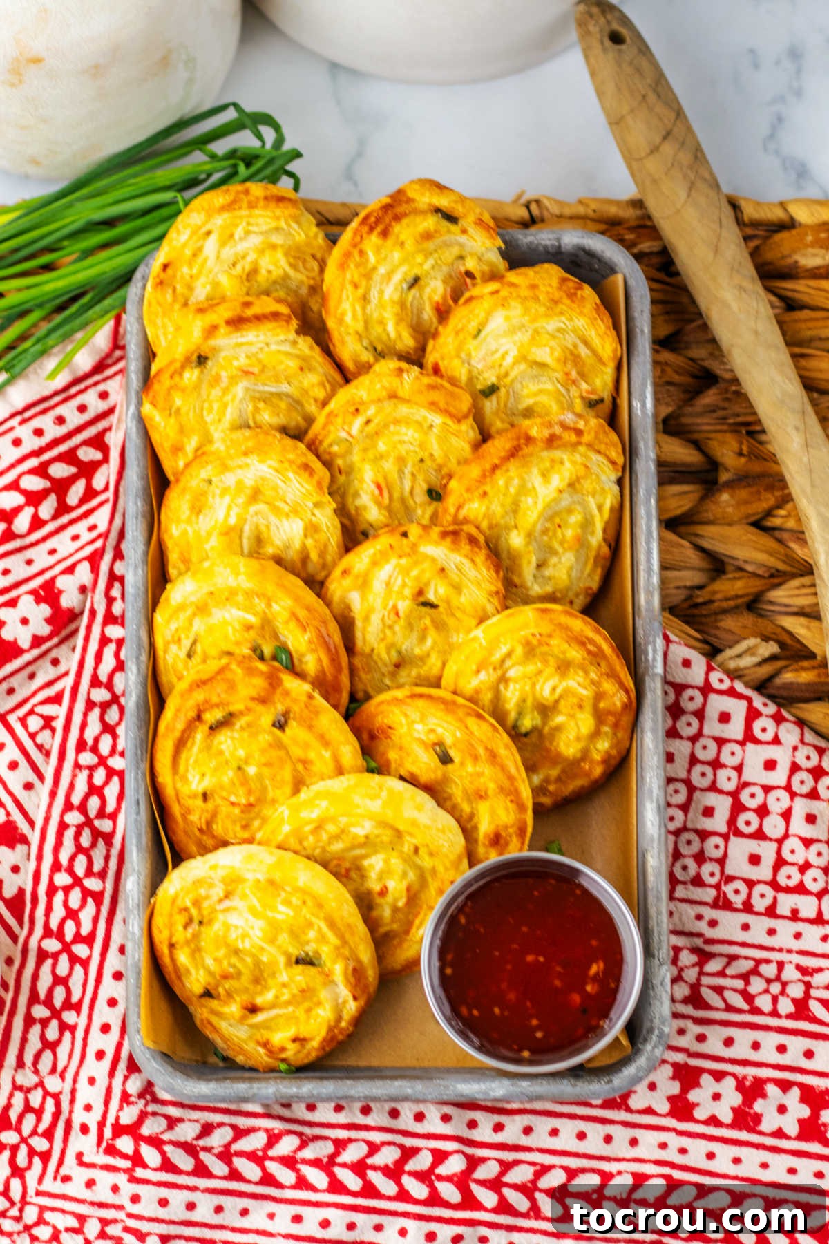 Small tray filled with baked crab rangoon pinwheels and a ramekin of chili sauce, ready to be served.