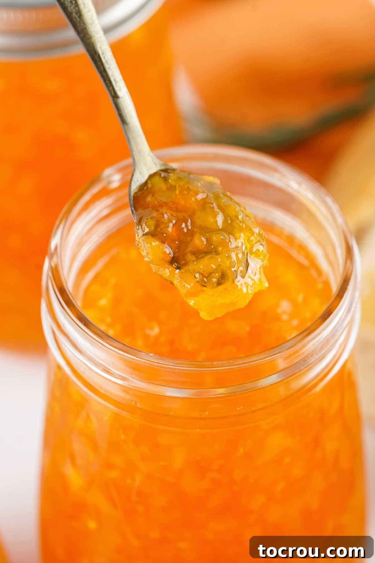 Sun-Kissed Orange Marmalade 4 Spoon lifting out a scoop of thick homemade orange marmalade with flecks of orange rind inside.