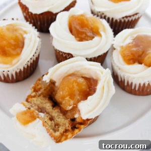A platter of apple pie filled cupcakes, with one cupcake broken open to reveal its delicious spiced apple filling inside.