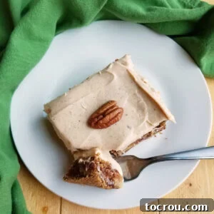 A perfect bite of German apple cake covered with luscious cinnamon brown sugar cream cheese frosting and topped with a pecan half.