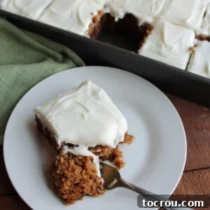 A fork taking a bite of Grandma's applesauce cake, showing its rich brown color from cinnamon, cloves, and allspice, with raisins visible inside and a swirl of cream cheese frosting on top.