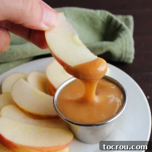 A crisp apple slice gracefully dipped into a container of rich, homemade caramel sauce.