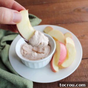 A hand holds a crisp apple slice generously coated with a smooth and creamy apple butter dip, ready for a delightful bite.