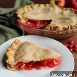 A vibrant slice of red hot candy apple pie, showcasing a bright red apple filling on a plate, with the rest of the pie visible in the background.