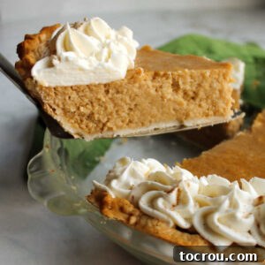 The first slice of apple butter pie being lifted out, showcasing its smooth, creamy filling and a dollop of whipped cream topping.
