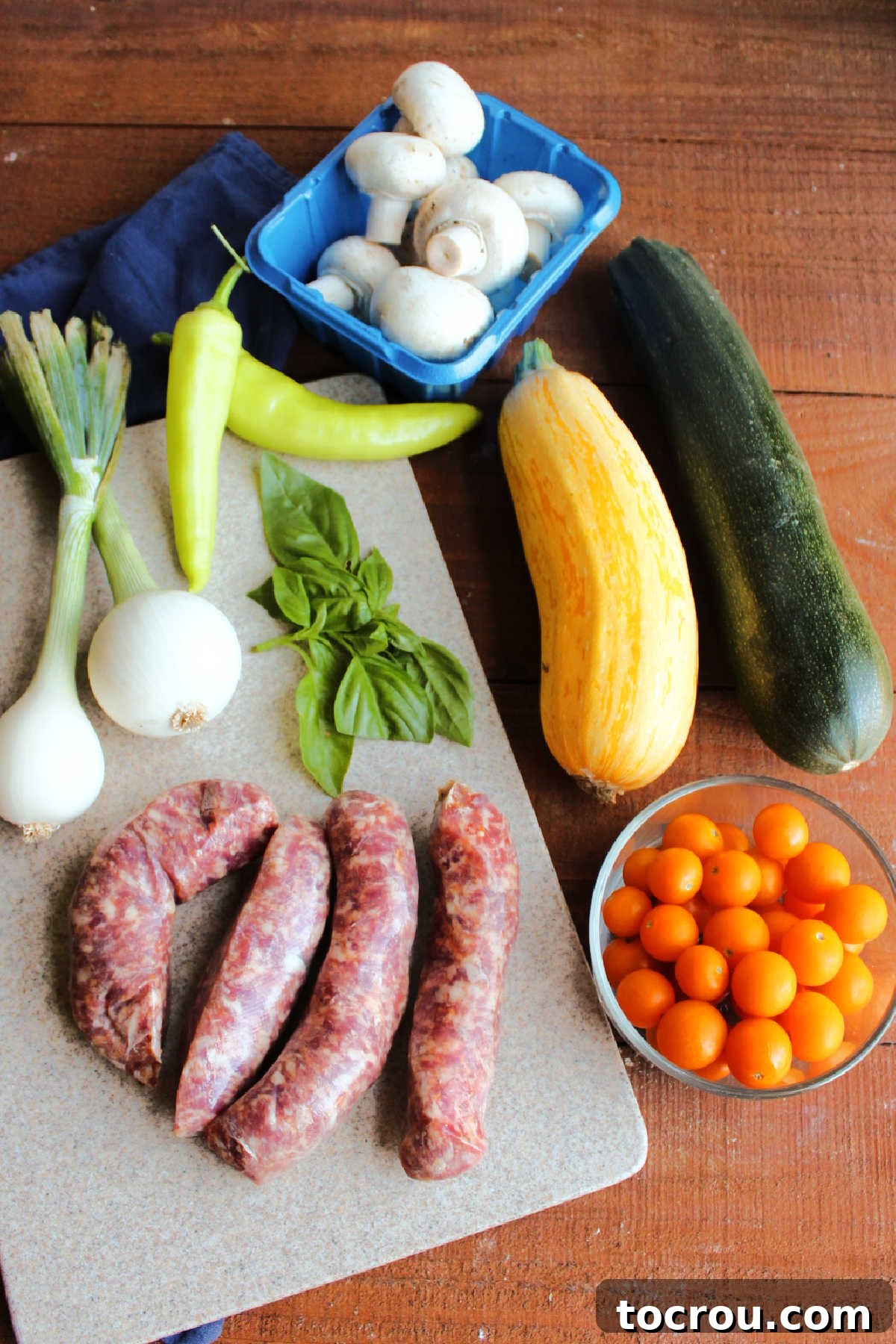One-Pan Italian Sausage and Roasted Vegetables 3 Ingredients including Italian sausage links, zucchini, yellow squash, cherry tomatoes, basil, spring onions, banana peppers and button mushrooms ready to be made into sheet pan meal.