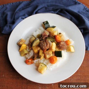 Dinner plate with rice under roasted Italian sausage chunks and vegetables including zucchini, yellow squash, cherry tomatoes, and more.