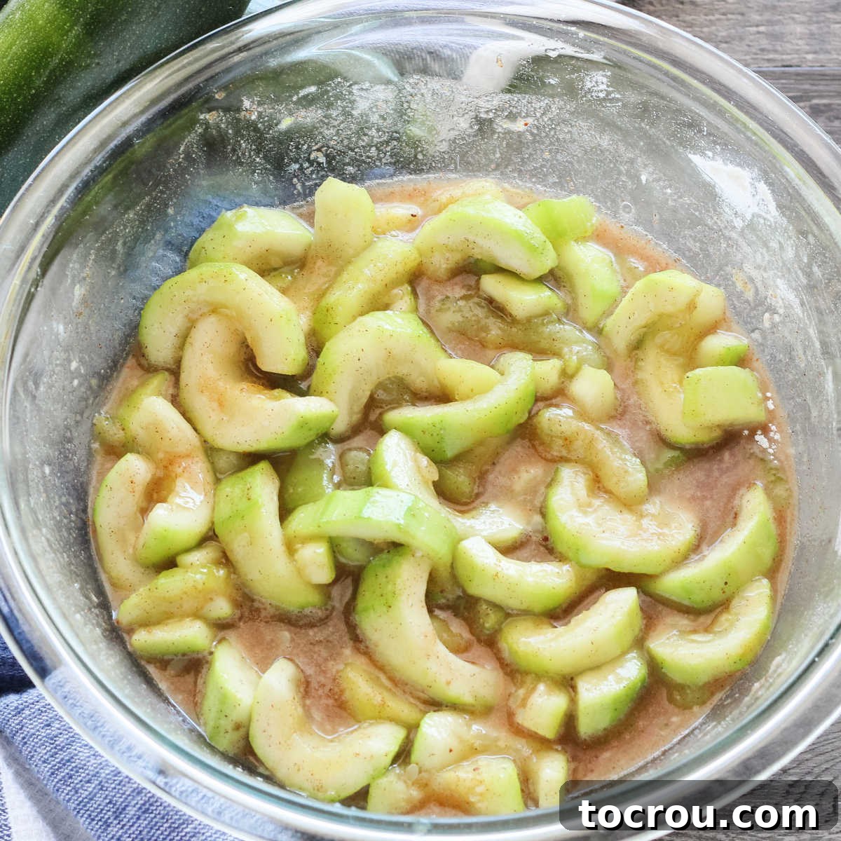 bowl of zucchini slices coated in cinnamon mixture ready to be baked into apple crisp like dessert.