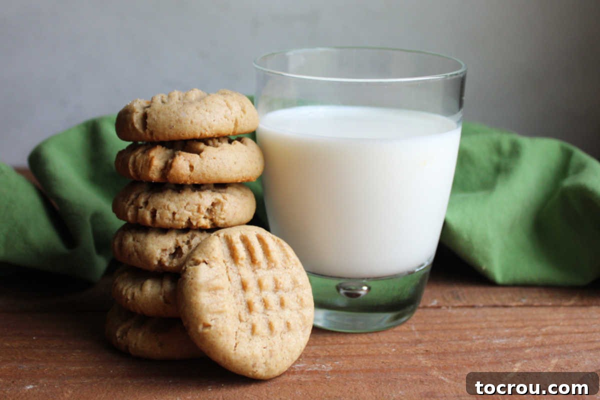 Stack of homemade peanut butter sourdough cookies with fork marks on top by a glass of milk, ready to be eaten. A classic, inviting scene.